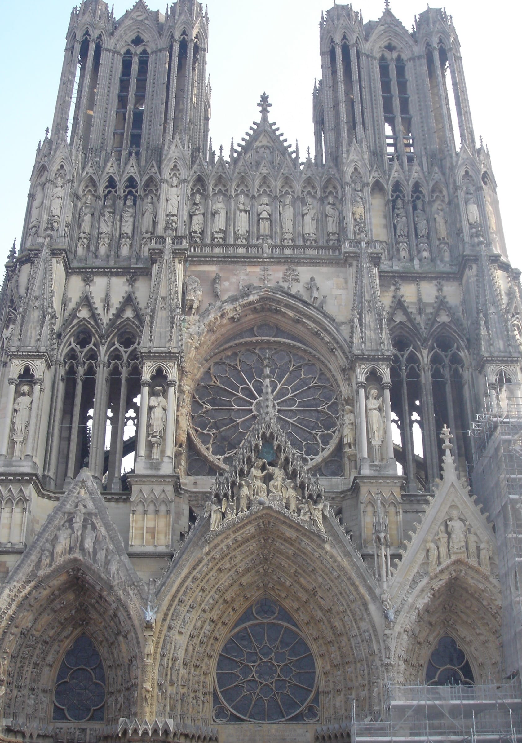 The façade of the cathedral at Reims, which is built of white stone. There are two towers, a rose window, and three portals with pointed arches.