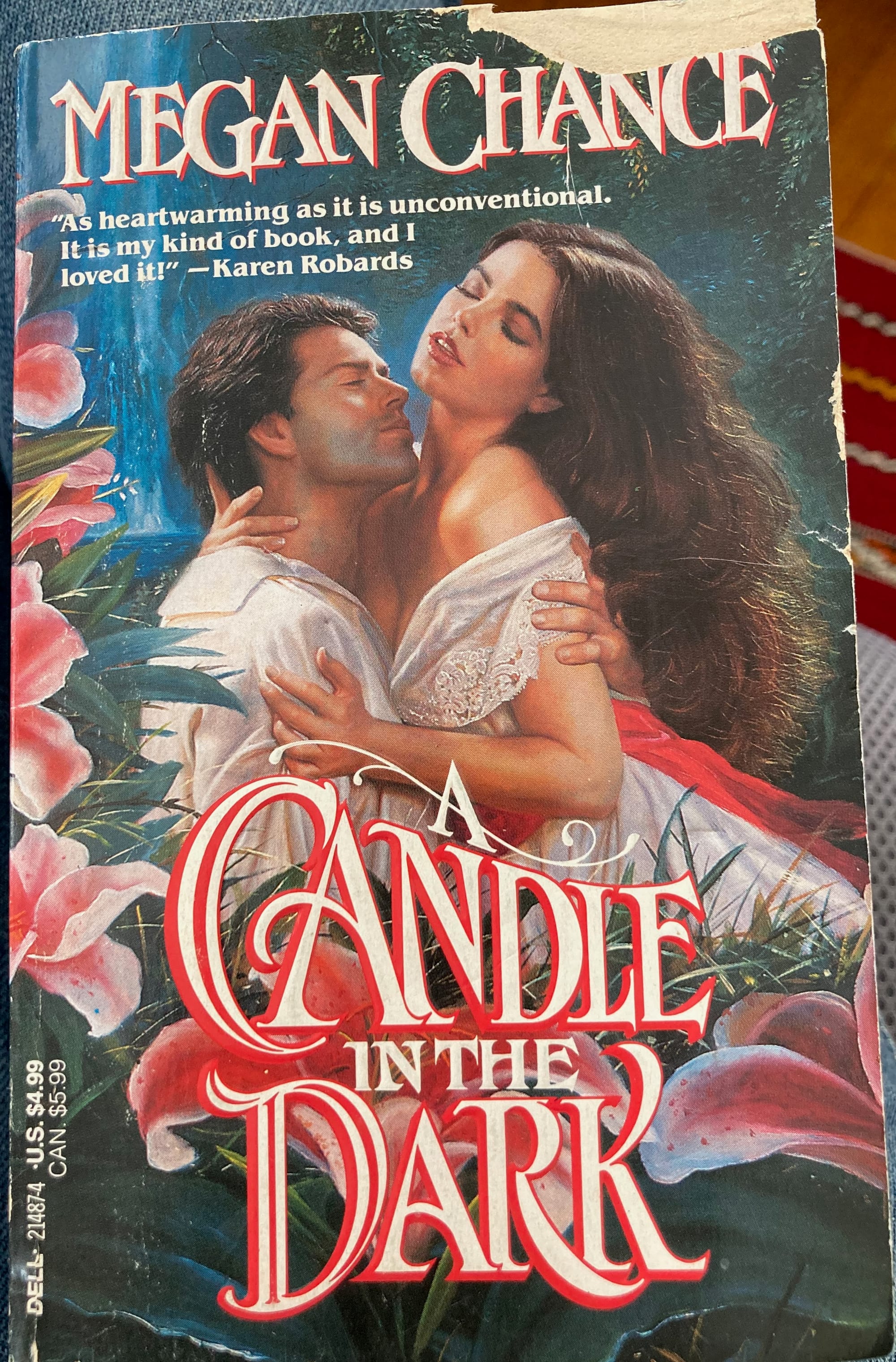 A slightly worn paperback copy of Megan Chance's A Candle in the Dark. The cover illustration shows a white man pulling a white woman into his lap to embrace her.