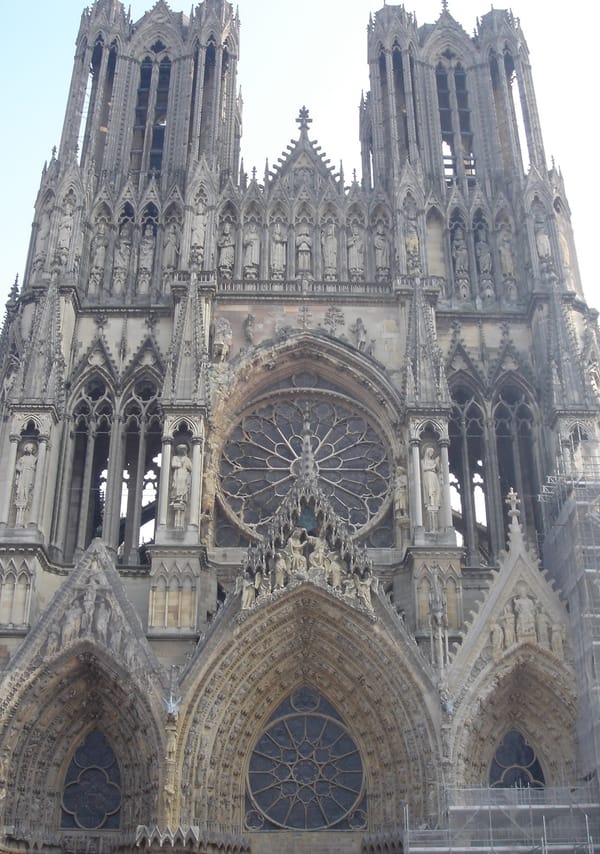 The façade of the cathedral at Reims, which is built of white stone. There are two towers, a rose window, and three portals with pointed arches.